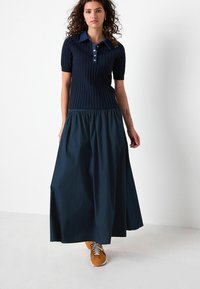 Marinblå tvådelad klänning med en ribbad poloöverdel med blå krage och korta ärmar, som leder ner till en flödig, rynkad maxikjol.