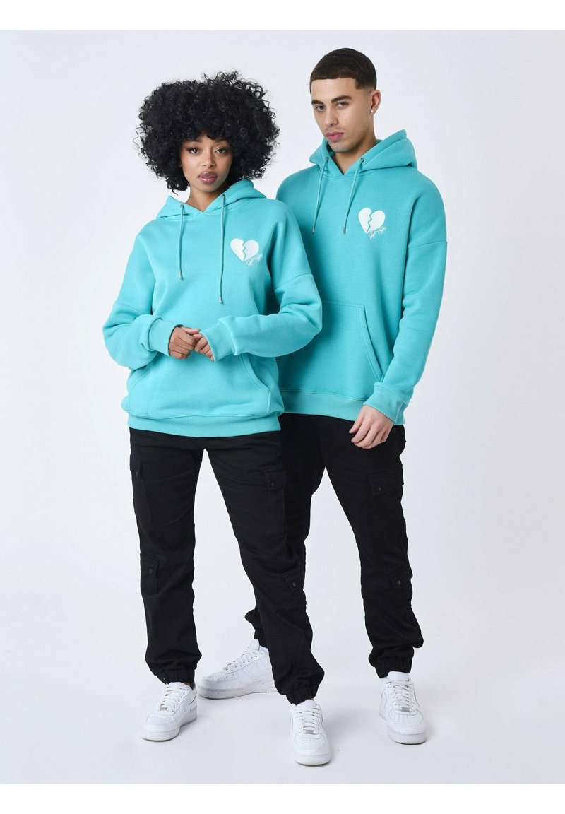 Sudaderas en color azul petróleo con gráfico de corazón blanco, bolsillos frontales y cordones; combinadas con pantalones cargo negros y zapatillas blancas.
