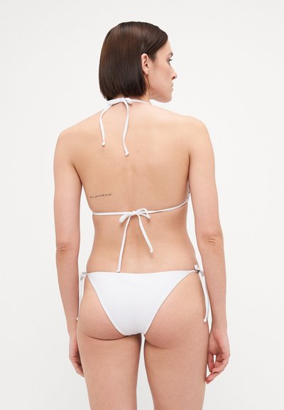 White bikini set featuring a tied halter neck top and adjustable side-tie bottoms, made from smooth fabric with minimalistic design.