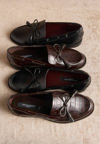 Mocasini din piele neagră și maro cu detaliu cu fundă, având texturi netede și embossate cu model de crocodil. Două perechi stivuite pe un fundal deschis.