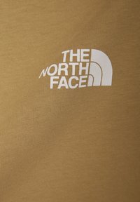 Puuvillapaita sinapinkeltaisena, jossa on edessä valkoinen "The North Face" -logo. Sileä pinta, istuva muotoilu.