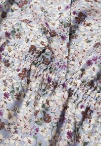 Tissu bleu clair avec élastique froncé, imprimé de petits motifs floraux blancs, marron, violets et verts.