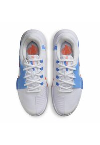 Zapatillas deportivas blancas con parte superior de malla, acentos azules, logo rojo en la lengüeta y cordones blancos. Suela texturizada con un diseño estructurado.