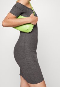 Robe grise côtelée épaules dénudées avec une silhouette ajustée, associée à un sac à main vert citron brillant avec une forme courbée et une sangle courte.