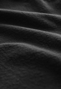 Tejido negro con una textura suave, mostrando pliegues suaves y fluidos, así como sutiles variaciones en el brillo. Sin patrones ni acentos visibles.