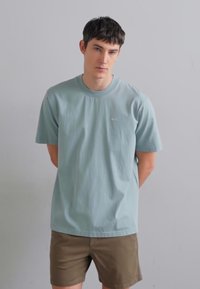 Lys blå T-skjorte med kort arm laget av bomull, med rund hals og en liten logo på brystet. Brukt med khaki shorts.
