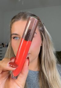 L'Oréal Paris lipgloss in een levendige koraalkleur met een glanzende afwerking. De tube heeft een roségouden dop en een doorzichtige onderkant.