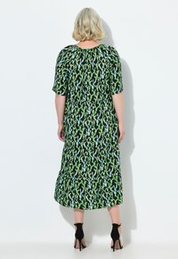 Schwarzes Kleid mit grünem und blauem Kaktusdruck, kurze Ärmel, geraffter Ausschnitt, knielange Länge, kombiniert mit schwarzen High-Heels.