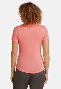 Camiseta de manga corta de color rosa, hecha de una tela suave, con un escote redondo y un dobladillo curvado en la parte posterior. Sin patrones visibles ni hardware.