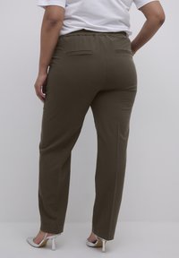 Braune elastische Bundhosen mit zwei Gesäßtaschen, geraden Beinen und einer glatten Textur. Getragen mit silbernen High Heels.