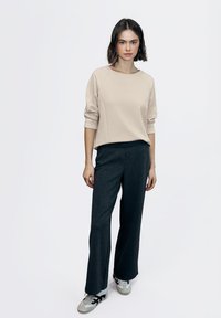 Sudadera beige con mangas raglán, combinada con pantalones anchos de rayas finas en color oscuro. Zapatillas con detalles en negro completan el conjunto.