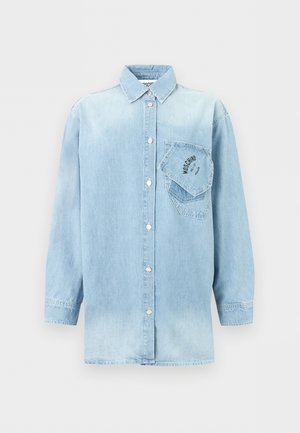 Chemise en denim bleu clair à manches longues avec fermeture à boutons et deux poches poitrine superposées, dont une inclinée avec un logo texte noir.
