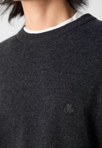 Dunkelgrauer Pullover mit Rundhalsausschnitt, strukturiertem Stoff und dezentem gesticktem Logo auf der Brust. Glattes und figurbetontes Design.