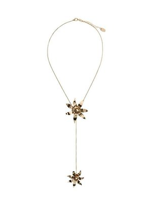 Collana dorata con due ornamenti floreali; più grande in alto, più piccolo in basso. Design della catena con motivi intricati su ciascun fiore.