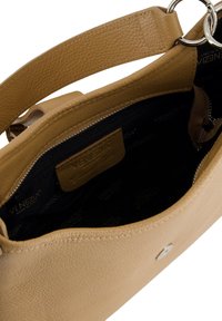Sac à main en cuir texturé beige avec une large bandoulière, des accents en anneau argenté et un intérieur en tissu noir comprenant une poche zippée et une étiquette de marque.