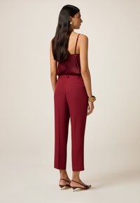Burgunderfarbendes ärmelloses Oberteil mit dünnen Trägern, kombiniert mit taillierten burgunderfarbenen Hosen. Das Outfit zeichnet sich durch eine glatte Textur und ein minimalistisches Design aus.