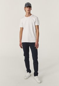 Witte katoenen t-shirt gecombineerd met marineblauwe chinos en witte sneakers. De pet heeft een donker, patroonontwerp met tinten grijs en marineblauw.