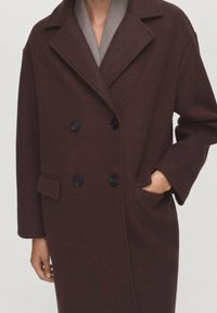 Cappotto in lana marrone a doppio petto con rever, grandi bottoni neri e tasche laterali; morbida trama e silhouette dritta.