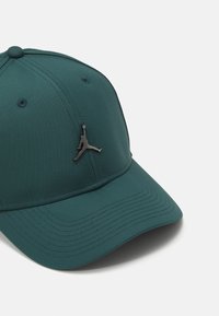 Tamna zelena kapa sa struktuiranim dizajnom, izrađena od teksturirane tkanine. Ima crni Jumpman logo sprijeda i zakrivljenu vizir.