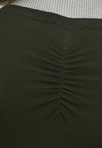 Detail zeleného žebrovaného svetru s nasbíraným designem vzadu. Látka je texturovaná a elastická, s jemným prošíváním.