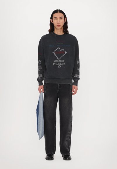 Sweatshirt noir surdimensionné avec des graphismes imprimés et du texte. Associé à un jean noir ample et tenant un sac en denim. Texture lisse, design décontracté.