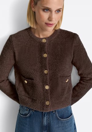 Braune strukturierte Jacke mit Rundhalsausschnitt, goldenen Knöpfen auf der Vorderseite und zwei vorderen Taschen. Tragen mit Jeans.