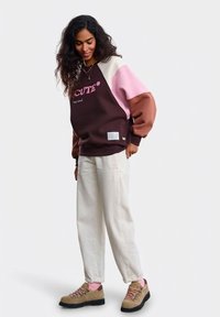 Ruda, rožinė ir smėlio spalvos marškinėliai blokuotu raštu su tekstu „GRAŽU*“; derinami su kremine kelnių pora ir rudais žygio batais su rožinėmis raištelėmis.