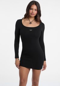 Schwarzes Langarm-Minikleid aus geripptem Stoff, mit einem runden Ausschnitt und einem kleinen Logo auf der Brust. Glatte Textur und figurbetonte Silhouette.