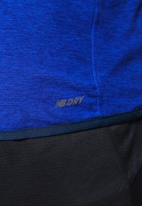 Blå atletisk tyg med en texturerad yta, med en svart nedre del och en gold "NB DRY" logotyp ovanför sömmen.