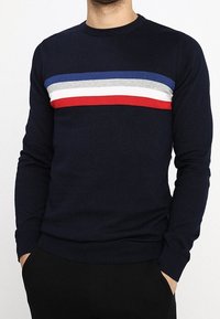 Mörkblå stickad tröja med rund halsringning, med horisontella ränder i blått, grått, vitt och rött över bröstet. Komfortanpassad design.