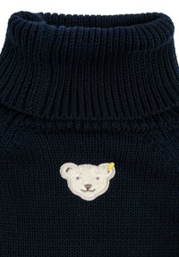 Golf turtleneck blu navy con texture a costine. Presenta un patch di testa d'orso crema con accenti gialli. Materiale morbido e accogliente.