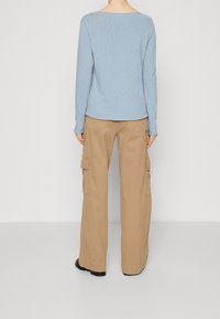 Světle modrý dlouhý rukáv s širokým výstřihem v kombinaci s béžovými cargo kalhotami, které mají boční kapsy a uvolněný střih. Celkově jednofarebný vzhled.