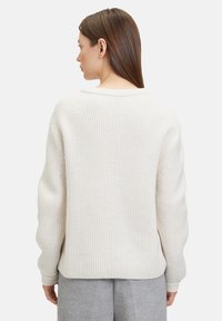 Fülliger, cremefarbener Strickpullover mit einem gerippten Muster, weitem Rundhalsausschnitt und überschnittenen Schultern. Lockerer Schnitt mit langen Ärmeln und gerader Silhouette.