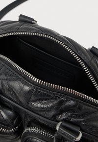 Melnas ādas izšūta rokassoma ar atvērtu sudraba rāvējslēdzēju, kurā redzama tukša iekšpuse un siksnu detaļas.