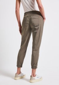 Pantalons tapered beige avec une taille élastique, des chevilles retroussées et des poches arrière visibles. Associés à des baskets blanches avec des accents beiges.