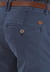 Námorné modré chinos nohavice s hnedými koženými detailmi, s gombíkovým zapínaním, zadnou vreckom a malou koženou nášivkou.