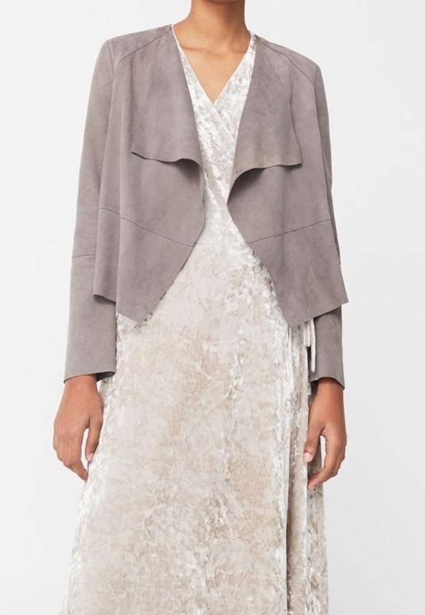 Femme portant une robe portefeuille beige clair texturée avec une veste grise douce drapée à ouverture devant, debout devant un fond uni.