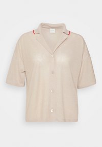Chemise beige à manches courtes avec boutons, col ouvert et petits accents rouges sur les épaules.