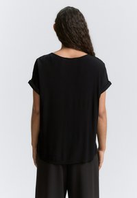 Haut noir à manches courtes, à coupe décontractée, avec un col rond et des manches retroussées. Fabriqué en tissu léger, texture lisse.