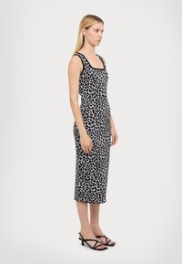 Midi haljina s uzorkom leopard kožne boje u crno-bijeloj, prilagođenog kroja, kvadratnog dekoltea, izrađena od mekanog materijala, uparena s crnim sandalama s remenčićima i visokom potpeticom.