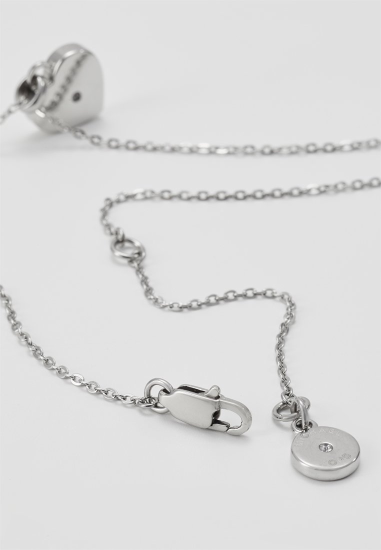 Silberne Metallkette mit einem herzförmigen Verschluss, Kettengliedern und einem runden Anhänger mit einem kleinen klaren Stein und Gravur.