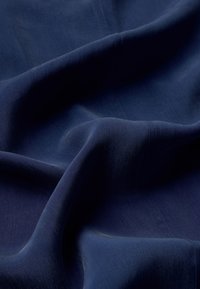 Donkerblauwe stof met een gladde, iets glanzende textuur, die zachte plooien en subtiele lichte reflecties toont, zonder zichtbare patronen of hardware.