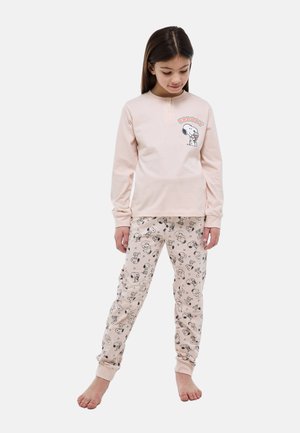 Fille portant un haut à manches longues rose clair à thème Snoopy et un pantalon assorti avec des motifs Snoopy, debout pieds nus sur un fond blanc.