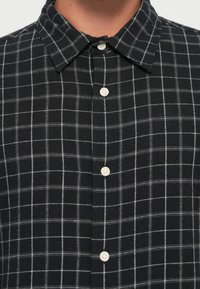 Czarna i biała koszula w kratkę z kołnierzykiem zapinanym na guziki, z białymi guzikami i miękkim, teksturowanym materiałem.