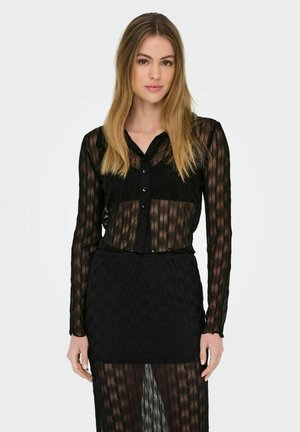 Blusa nera trasparente in tessuto nero strutturato, maniche lunghe, chiusura a bottoni e una gonna coordinata. Il motivo presenta linee ondulate.