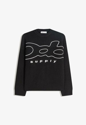 Svart tröja med vit grafisk design och texten "supply", ribbade muddar och fåll, gjord av ett mjukt stickat material.