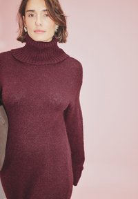 Burgundi värvi kootud sviiter kõrge ribataskuga, pikkade varrukatega ja lõdva lõikega. Pehme tekstuur kergelt läikiv.