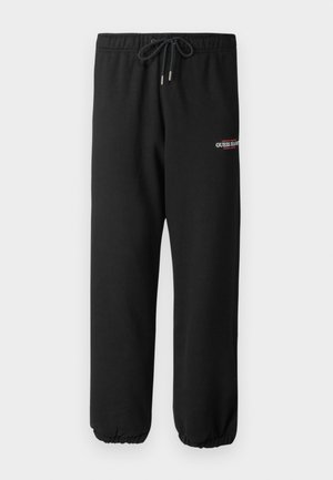 Pantaloni della tuta neri realizzati in tessuto morbido, con vita elastica dotata di cordino e polsini elastici, con logo "GUESS JEANS" in bianco e rosso.