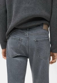 Vaqueros de mezclilla grises con un diseño de cintura alta, que cuentan con dos bolsillos traseros y una tela texturizada. En la cinturilla se observa una etiqueta de cuero marrón.