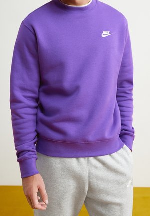 Sudadera morada de manga larga, con puños y escote acanalados. Presenta un pequeño logo blanco de Nike en el pecho, combinado con pantalones de chándal grises.